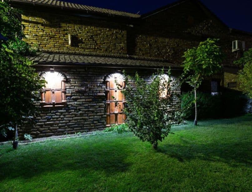 Pokošena trava i malo dekorativno drveće sa ciglenom konstrukcijom osvetljenom blagim svetlima na Camping Sosul noću